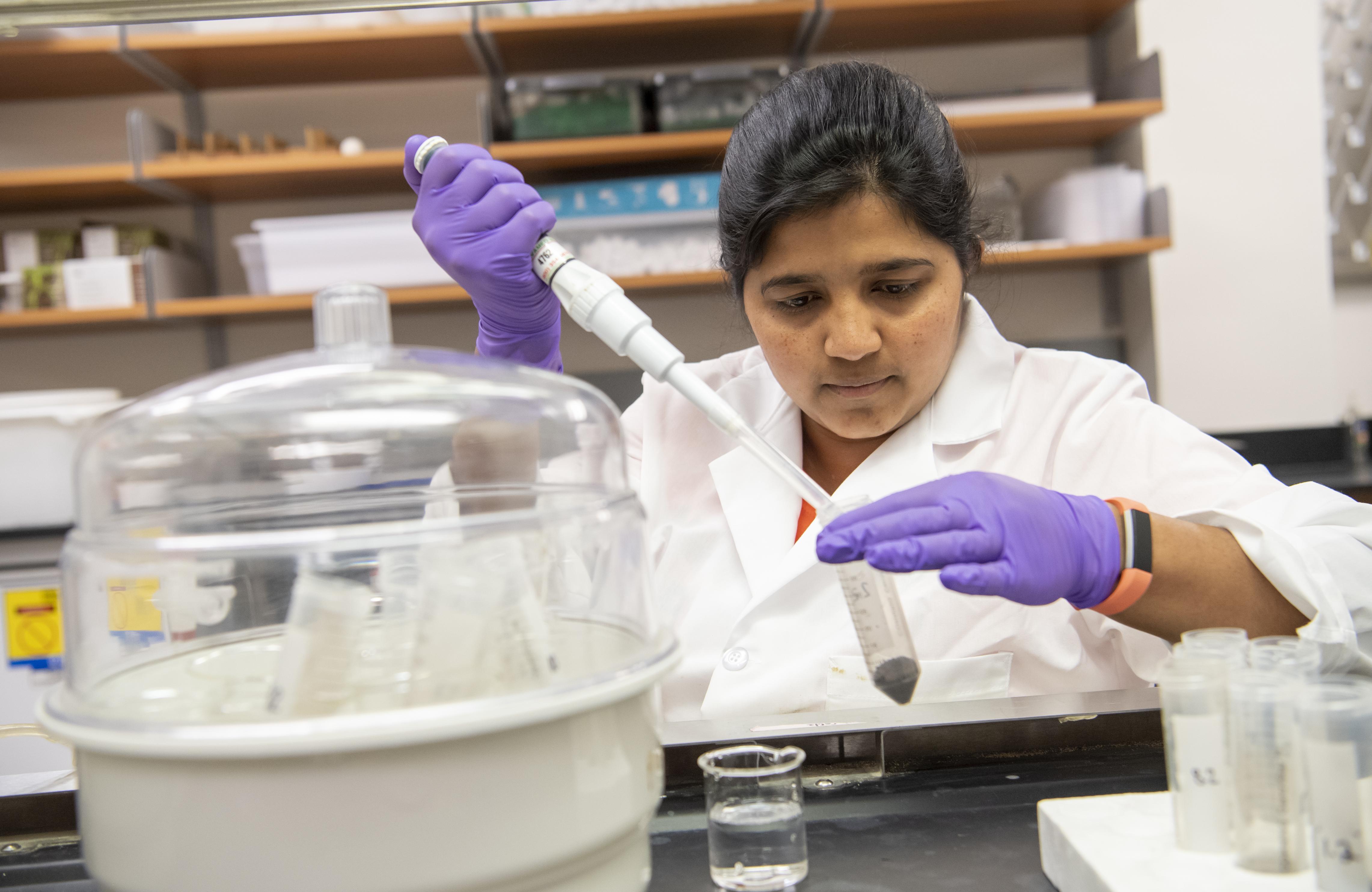 Graduate student using scientific equipment in lab to perform experiment
