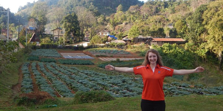 Study abroad student standing with their arms out in front of crops