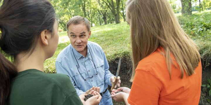 Professor examining soil with two students