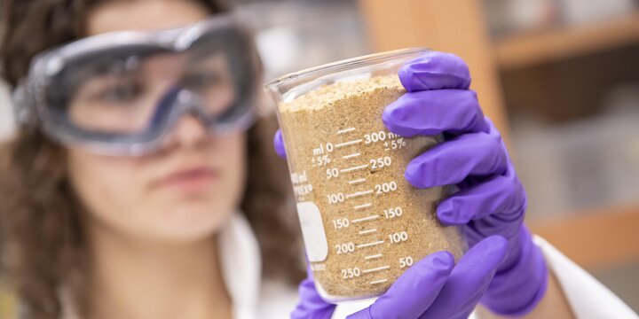 Student in a lab with goggles on examining a substance in a beaker.