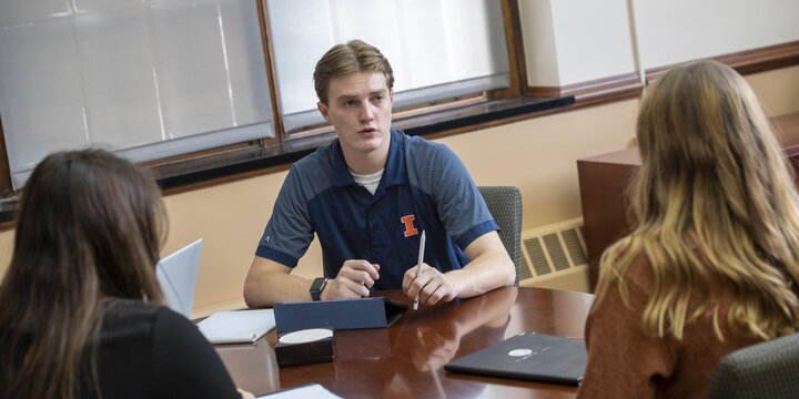 Three students sitting at a desk with the focus on the middle student