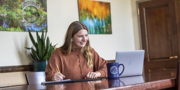 Student sitting at a desk working on a computer and writing in a notebook