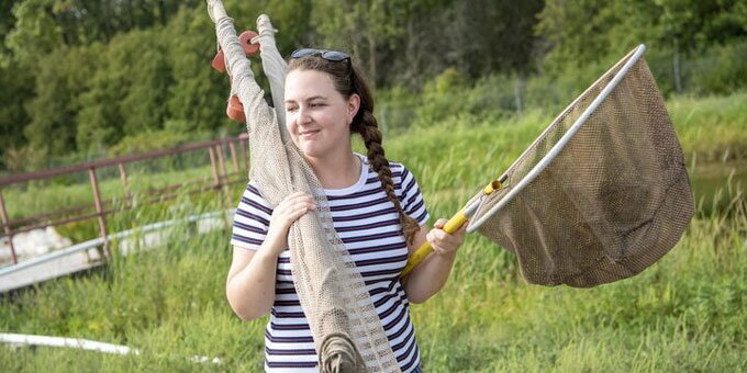 Student at river holding fishing nets.