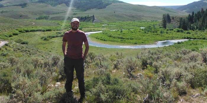 Student standing by grassy hills and a river